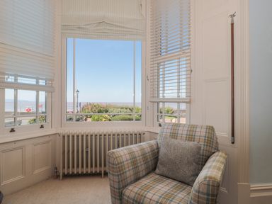 A corner room with large windows looking outside at the sea with a plaid armchair and a gray pillow at 49 Esplanade in Burnham-On-Sea