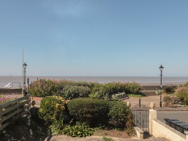 A garden with bushes and plants overlooking a promenade and the sea at 49 Esplanade in Burnham-On-Sea
