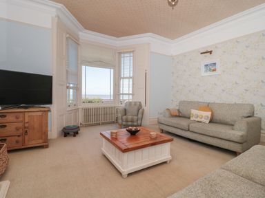 A living room with two gray sofas a wooden coffee table a patterned armchair a wooden cabinet with a television and a bay window at 49 Esplanade Burnham-On-Sea