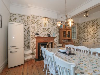 A dining room with a table and chairs near a wooden cabinet and refrigerator at 49 Esplanade in Burnham-On-Sea