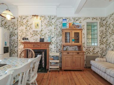 A dining area with a wooden table and chairs a wooden cabinet a fireplace with a mantle and a striped sofa at 49 Esplanade Burnham-On-Sea