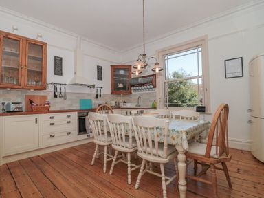 A kitchen with wooden floor cabinets a dining table with chairs and a window at 49 Esplanade in Burnham-On-Sea