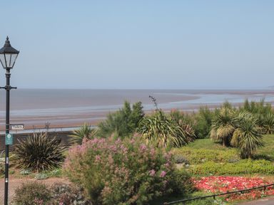 A seaside view with various green and flowering plants and a black street lamp with a sign pointing to toilets at 49 Esplanade in Burnham-On-Sea