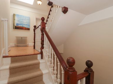 A staircase with beige carpet and wooden banister leading to a landing with wooden floor and radiator at 49 Esplanade in Burnham-On-Sea