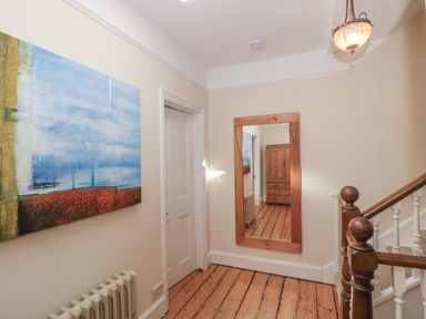 A hallway with wooden floor a wooden framed mirror a painting a radiator a closed door and wooden staircase at 49 Esplanade in Burnham-On-Sea