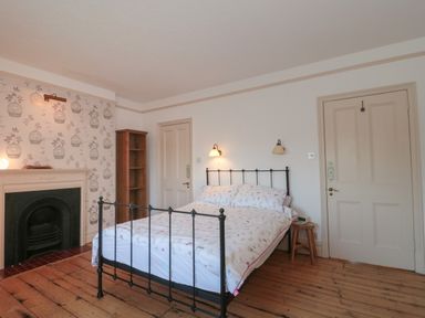 A bedroom with a double bed and two wall lamps a wooden floor and a fireplace at 49 Esplanade in Burnham-On-Sea