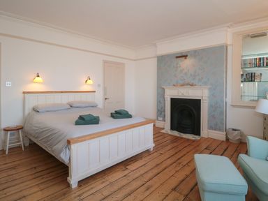 A bedroom with a bed beside a fireplace and a blue armchair at 49 Esplanade in Burnham-On-Sea