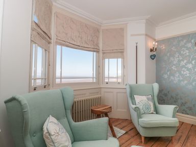 A sitting room with two armchairs and a wooden side table by bay windows at 49 Esplanade in Burnham-On-Sea