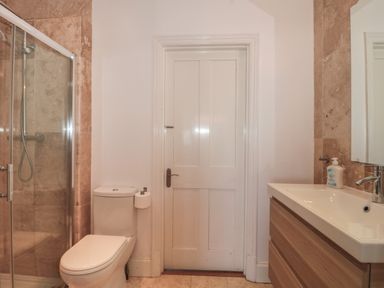 A bathroom with a toilet and shower on the left and a sink with a wooden cabinet and mirror on the right at 49 Esplanade in Burnham-On-Sea