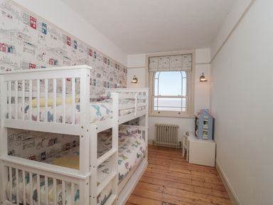 A children's bedroom with bunk beds a window radiator and a small dollhouse at 49 Esplanade in Burnham-On-Sea