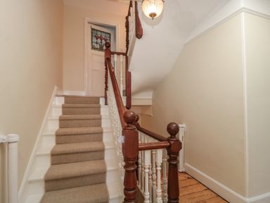 A staircase with beige carpet and wooden handrails leading to a door with stained glass panel at 49 Esplanade Burnham-On-Sea