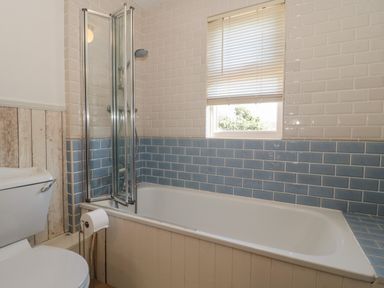 A bathroom with a bathtub shower combination a toilet and a window with blinds at 49 Esplanade in Burnham-On-Sea