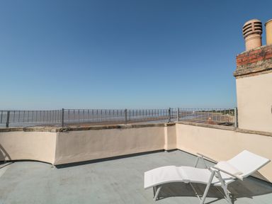 A rooftop terrace with a white lounge chair overlooking a beach and sea at 49 Esplanade in Burnham-On-Sea