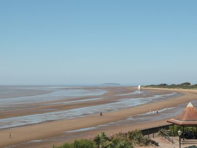 A beach with wet sand and shallow water with people walking and a pavilion near the shore at 49 Esplanade in Burnham-On-Sea