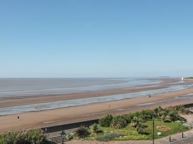 A beach with low tide revealing wet sand with a green landscaped area in the foreground at 49 Esplanade in Burnham-On-Sea