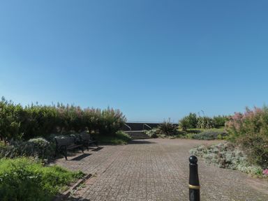 A paved outdoor area with benches bushes and stairs leading up to a railing at 49 Esplanade in Burnham-On-Sea