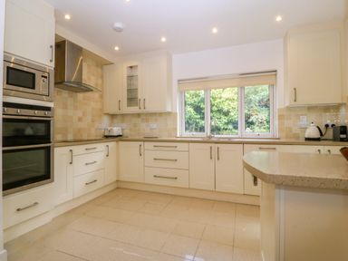 A kitchen with cream cabinets an oven microwave toaster kettle and a window showing greenery at Gwylanod in Llwyngwril near Fairbourne