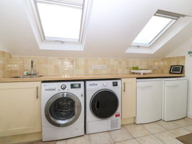 A laundry room with a washing machine dryer two white storage units and a sink under skylight windows at Gwylanod in Llwyngwril near Fairbourne