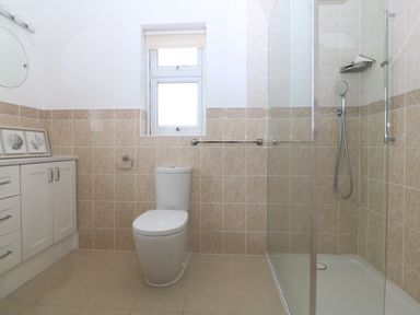 A bathroom with a toilet, shower enclosure, tiled walls, a window, and a cabinet with framed pictures at Gwylanod in Llwyngwril near Fairbourne