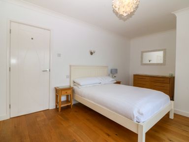 A bedroom with a white bed frame a bedside table wooden floor and a dresser with a mirror at Gwylanod Llwyngwril near Fairbourne