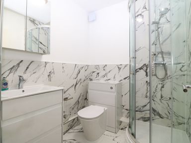 A bathroom with a toilet a sink a shower enclosure and marble patterned tiles at Gwylanod in Llwyngwril near Fairbourne