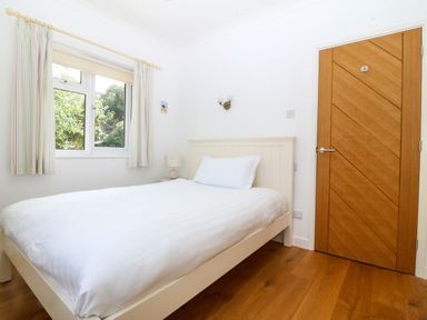 A bedroom with a white bed near a window and a wooden door at Gwylanod in Llwyngwril near Fairbourne