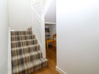 A staircase with striped carpet and a small desk with shelves underneath at Gwylanod in Llwyngwril near Fairbourne