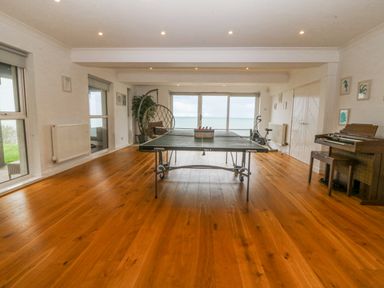 A room with a ping pong table a hanging chair and a piano with wooden flooring at Gwylanod in Llwyngwril near Fairbourne