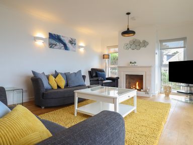 A living room with a fireplace a yellow rug a white coffee table and sofas at Gwylanod in Llwyngwril near Fairbourne