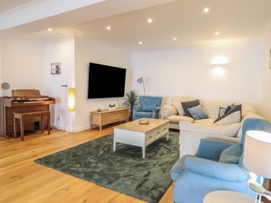 A living room with blue armchairs a beige sofa an organ a mounted television and a coffee table at Gwylanod in Llwyngwril near Fairbourne