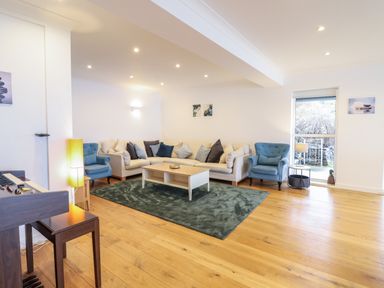 A living room with a large beige sectional sofa blue armchairs wooden floor and a piano at Gwylanod in Llwyngwril near Fairbourne