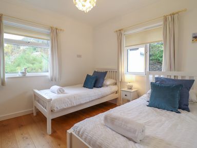 A bedroom with two single beds pillows bedside table with lamp and windows with curtains at Gwylanod in Llwyngwril near Fairbourne