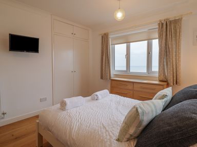 A bedroom with a bed two rolled towels a wooden dresser and a window with curtains at Gwylanod in Llwyngwril near Fairbourne