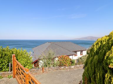 A house with a pitched roof by the sea with a wooden gate and greenery at Gwylanod in Llwyngwril near Fairbourne