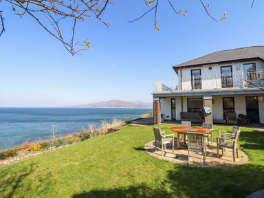 A house with a patio set on a grassy lawn overlooking the sea at Gwylanod in Llwyngwril near Fairbourne