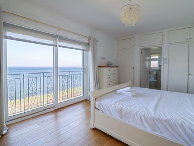 A bedroom with a bed towels on it and sliding glass doors overlooking the sea at Gwylanod in Llwyngwril near Fairbourne