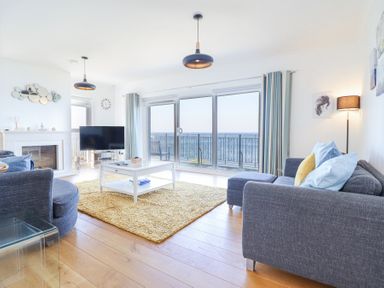 A living room with grey sofas a white coffee table a yellow rug a fireplace and large windows with sea view at Gwylanod in Llwyngwril near Fairbourne