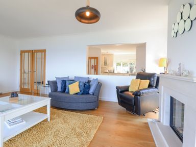 A living room with a blue sofa, black armchair, white coffee table, yellow rug, and fireplace at Gwylanod in Llwyngwril near Fairbourne