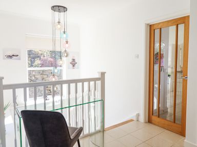 A hallway with a glass desk and chair near a wooden door with glass panels at Gwylanod in Llwyngwril near Fairbourne