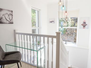 A stairway landing with a glass desk chair and hanging pendant lights at Gwylanod in Llwyngwril near Fairbourne