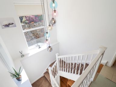 A stairway with brown carpet and white railing with a window and hanging pendant lights at Gwylanod in Llwyngwril near Fairbourne