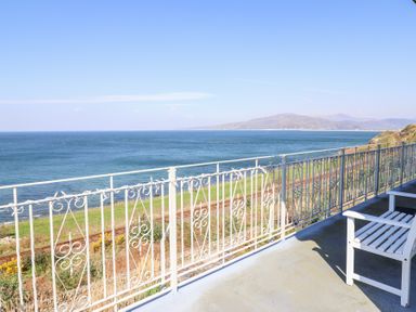 A balcony with white railing and chair overlooking the sea and distant hills at Gwylanod in Llwyngwril near Fairbourne