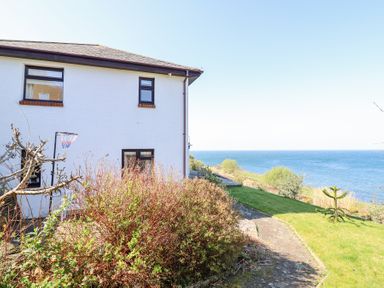 A side view of a white house with bushes and a basketball hoop near the coast at Gwylanod in Llwyngwril near Fairbourne