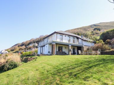 A two-story house with a balcony and outdoor seating on a grassy hill at Gwylanod in Llwyngwril near Fairbourne