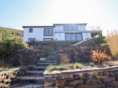 Stone steps leading up to a two-story house with white walls and balconies at Gwylanod Llwyngwril near Fairbourne