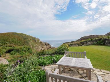 A garden area with wooden table and chairs overlooking the ocean at Pendower Cottage in Porthgwarra