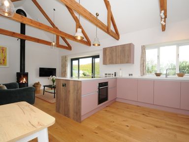 An open kitchen and living area with wooden beams wood flooring and a fireplace at Pendower Cottage in Porthgwarra