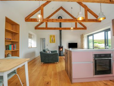 A kitchen and living area with wooden beams on the ceiling and a wood burning stove at Pendower Cottage in Porthgwarra