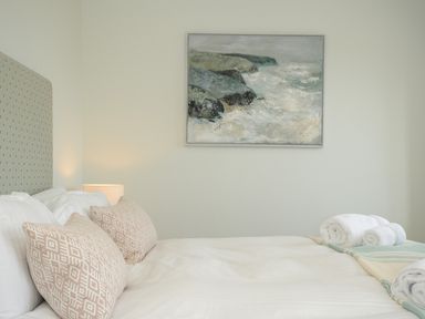 A bedroom with a bed with pillows and rolled towels and a painting on the wall at Pendower Cottage in Porthgwarra