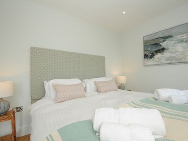 A bedroom with a double bed two bedside tables with lamps and rolled towels on the bed at Pendower Cottage in Porthgwarra